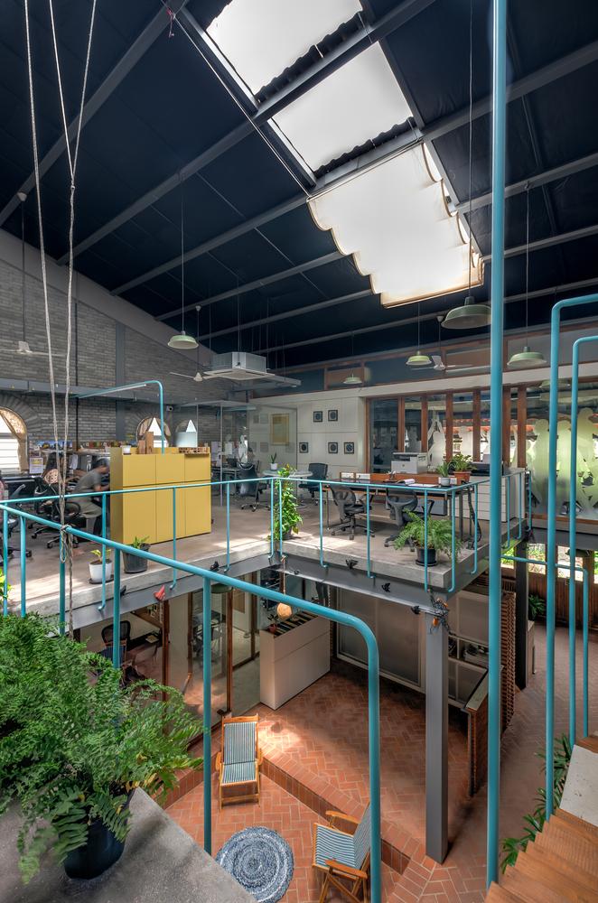 View from upper mezzanine through central skylight showing turquoise railings and potted plants on multiple levels