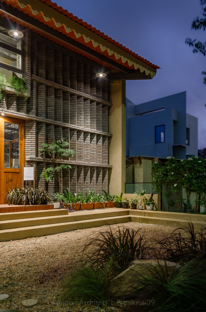 Exterior courtyard with terraced planters and horizontal brick facade under a scalloped roof at dusk