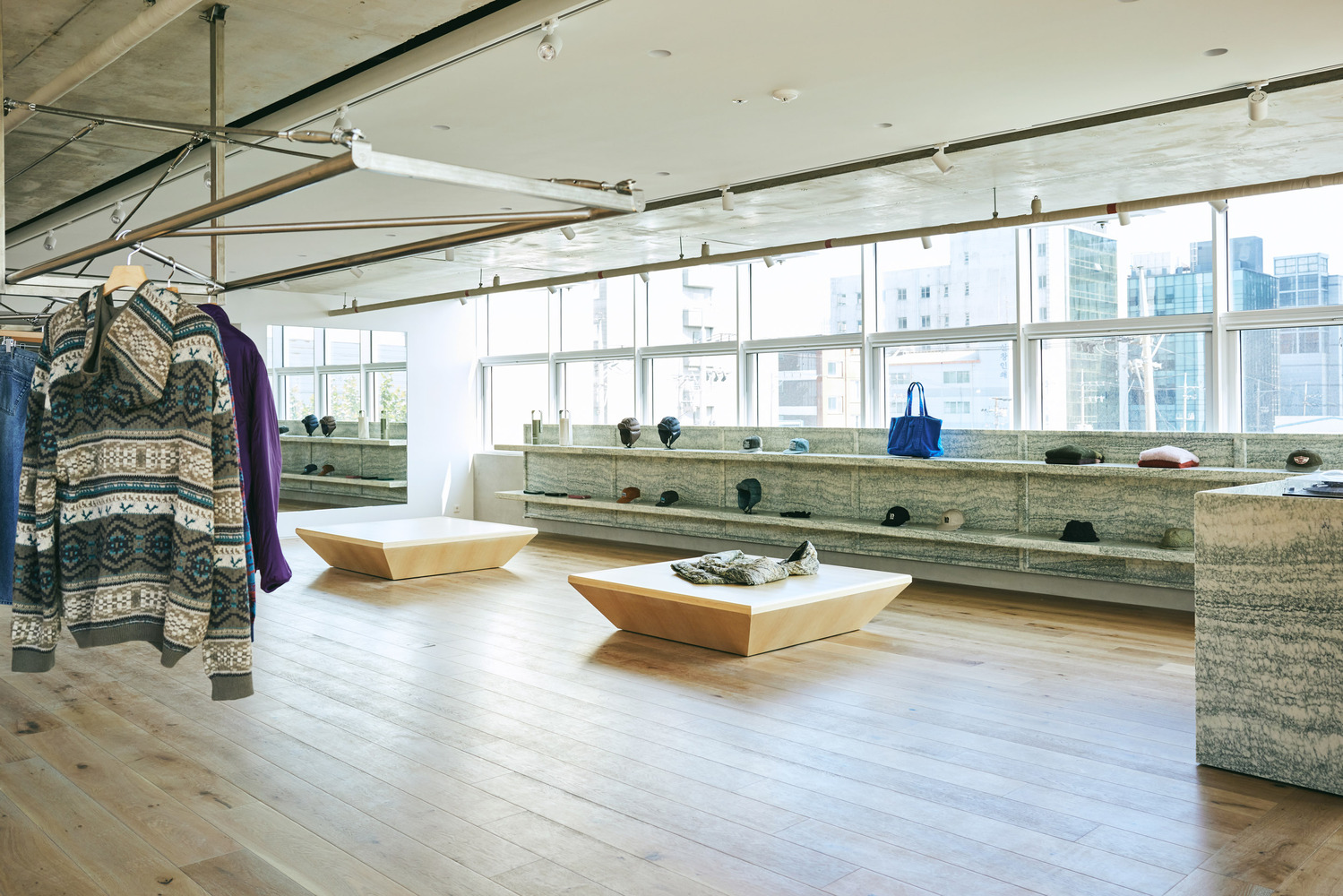 Main floor: stainless steel tension-wire hanging rail, plywood display tables, granite counter, caps and bags along window wall