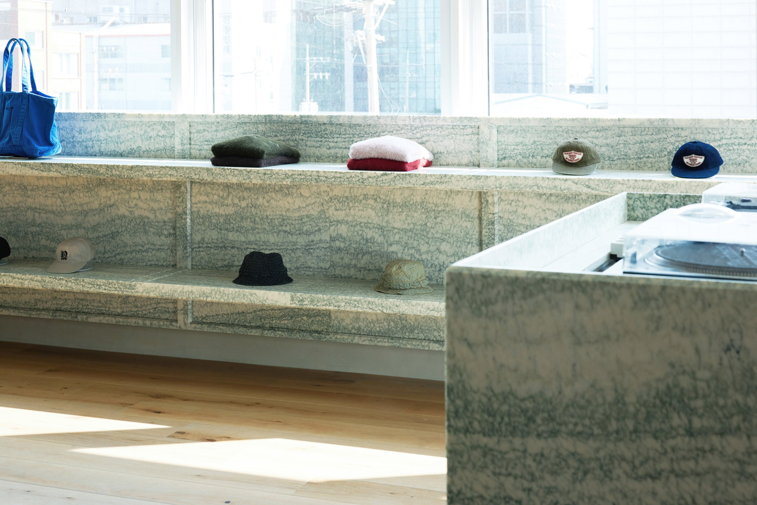 Granite display detail: layered stone shelves with caps, folded knitwear, blue bag, window light behind