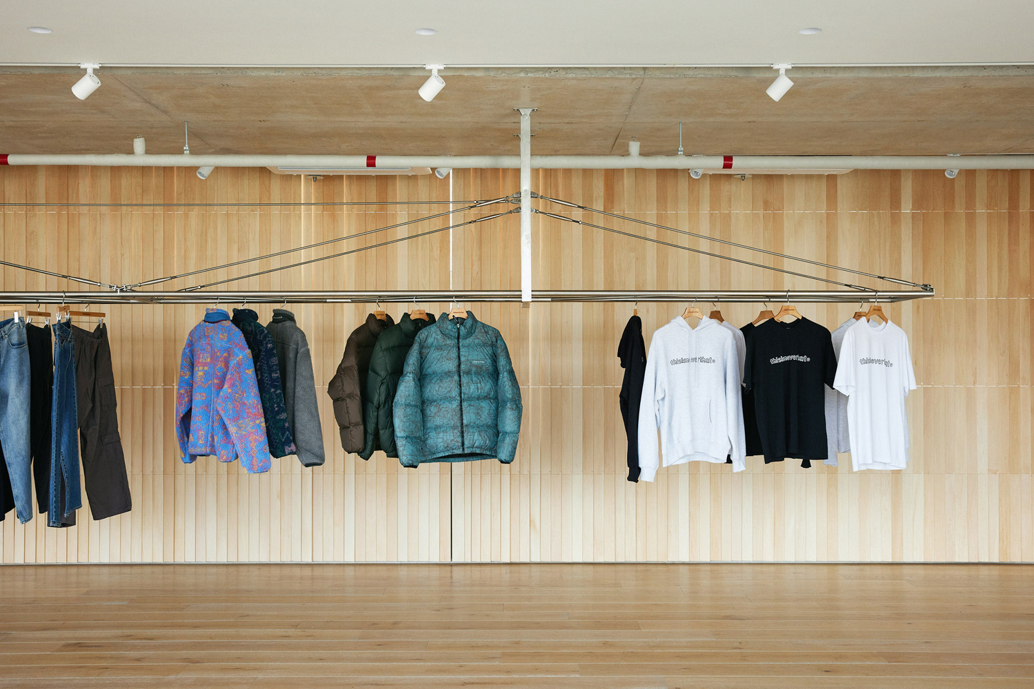 Outerwear display: jackets hung against the timber slat wall, oak floor, warm sidelight