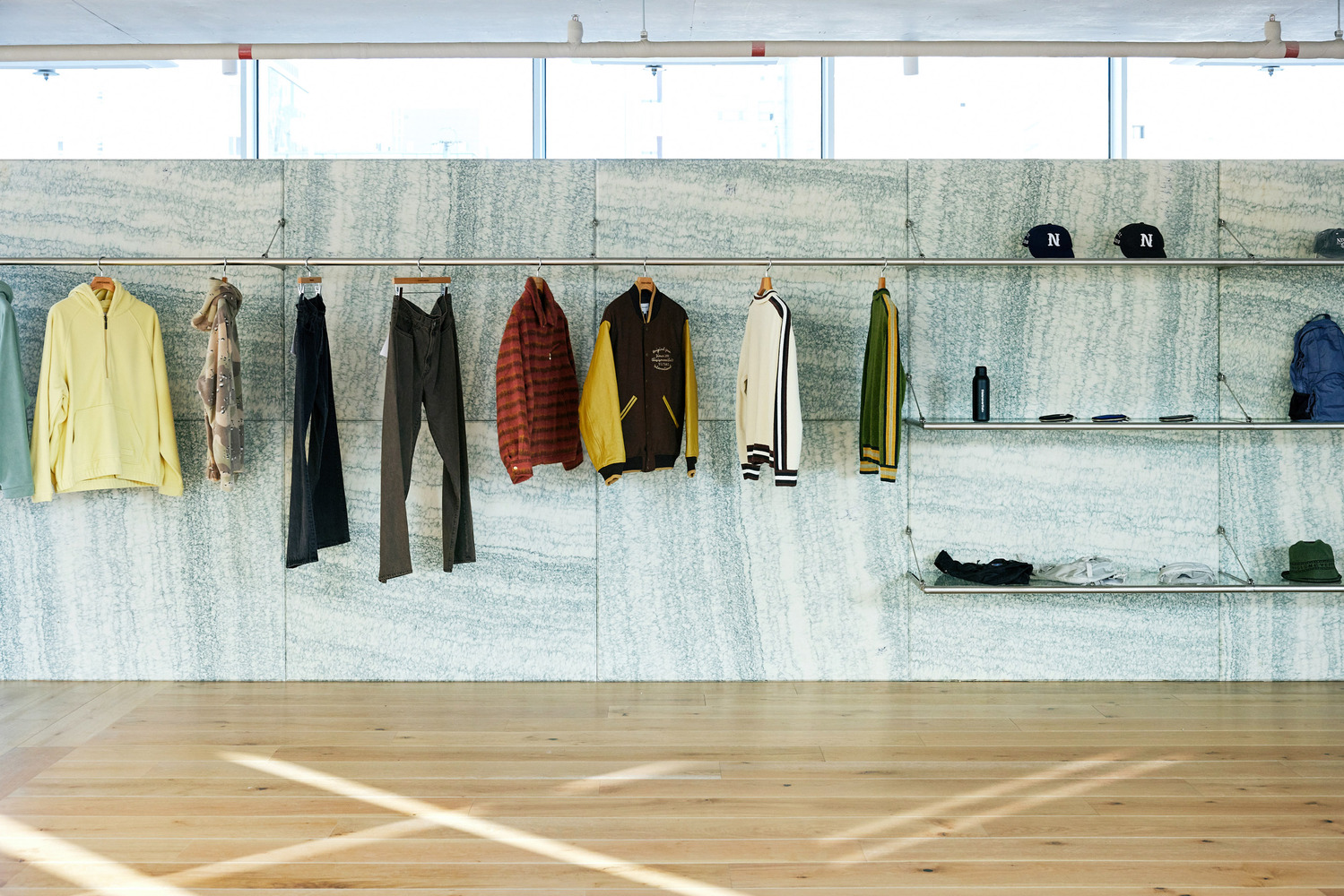 Perimeter display: clothing rails against granite-clad lower wall, oak floor, large industrial windows, track lighting