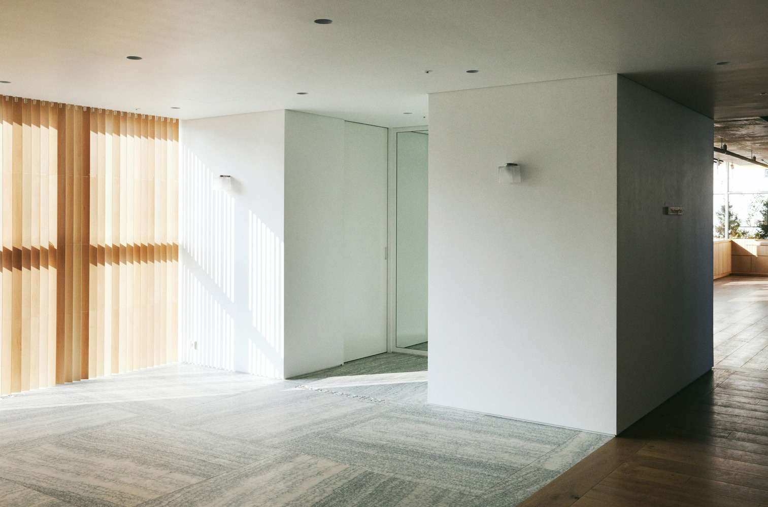 Corridor junction: white partition walls with openings framing display rooms, timber slat wall glowing beyond, granite floor