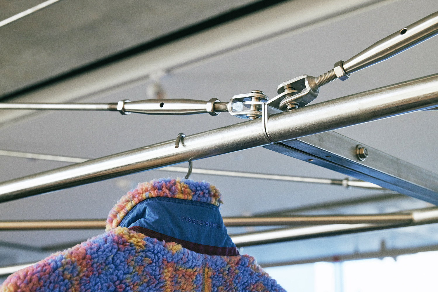 Rail detail: stainless steel turnbuckle and tension wire joint, fleece jacket hanging, exposed ceiling above