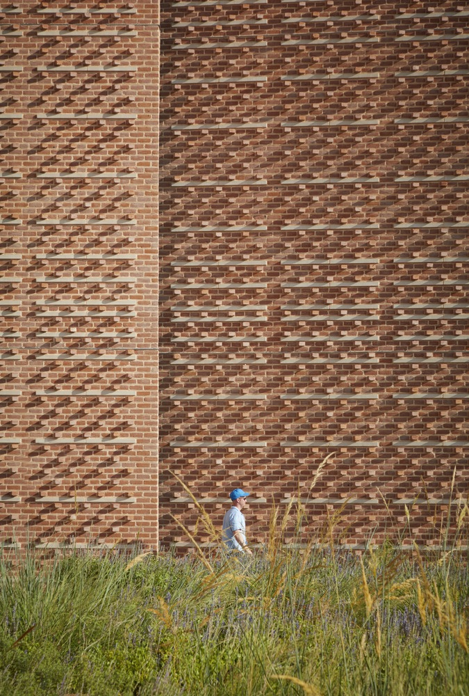 Brick facade with varied bond pattern behind tall grasses and person walking below