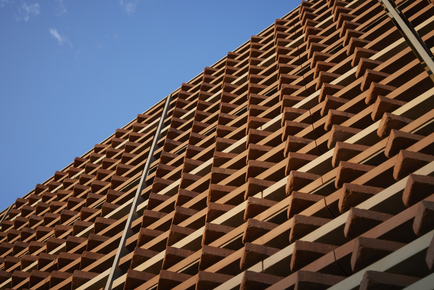 Upward view of terracotta louver screen in diagonal pattern against blue sky