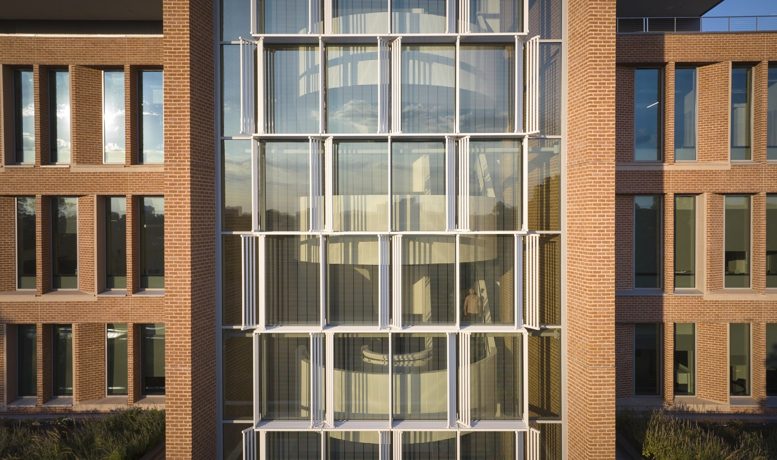 Central glass stair tower framed by brick wings with vertical window slots under clear sky