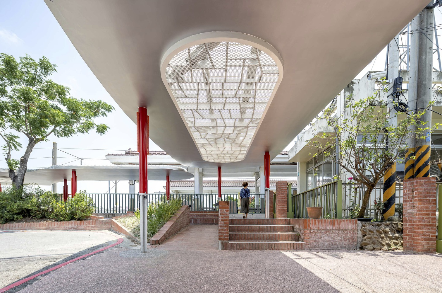 Under the canopy: large oval skylight with decorative metal screen, red columns, brick steps and ramp, figure walking