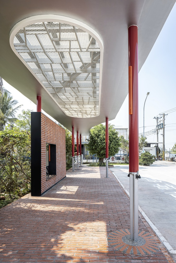 Covered walkway: red columns, oval skylight overhead, brick paving, trees along the edge