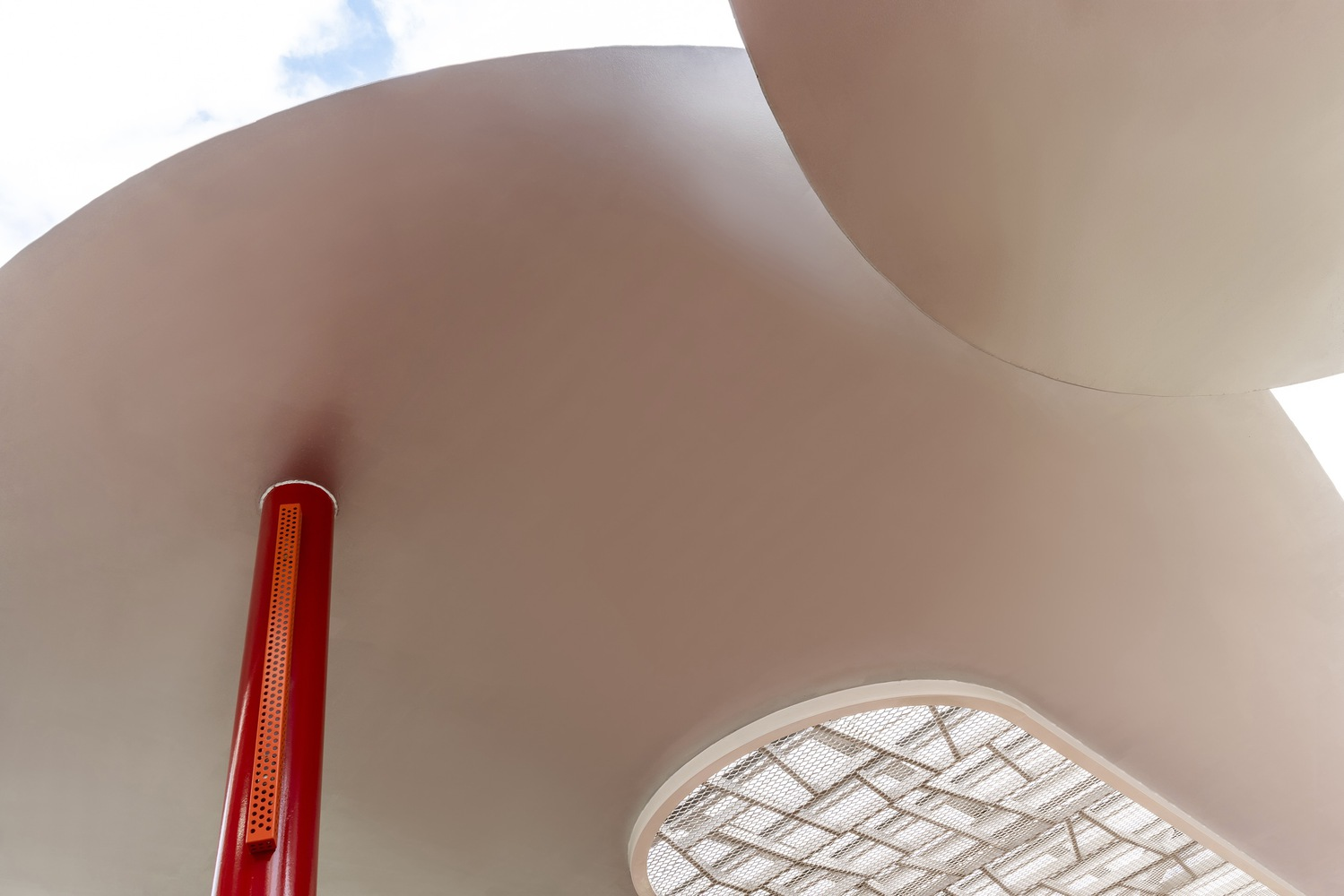 Underside detail: curved white concrete canopy meeting a red column, oval skylight with patterned metal screen above