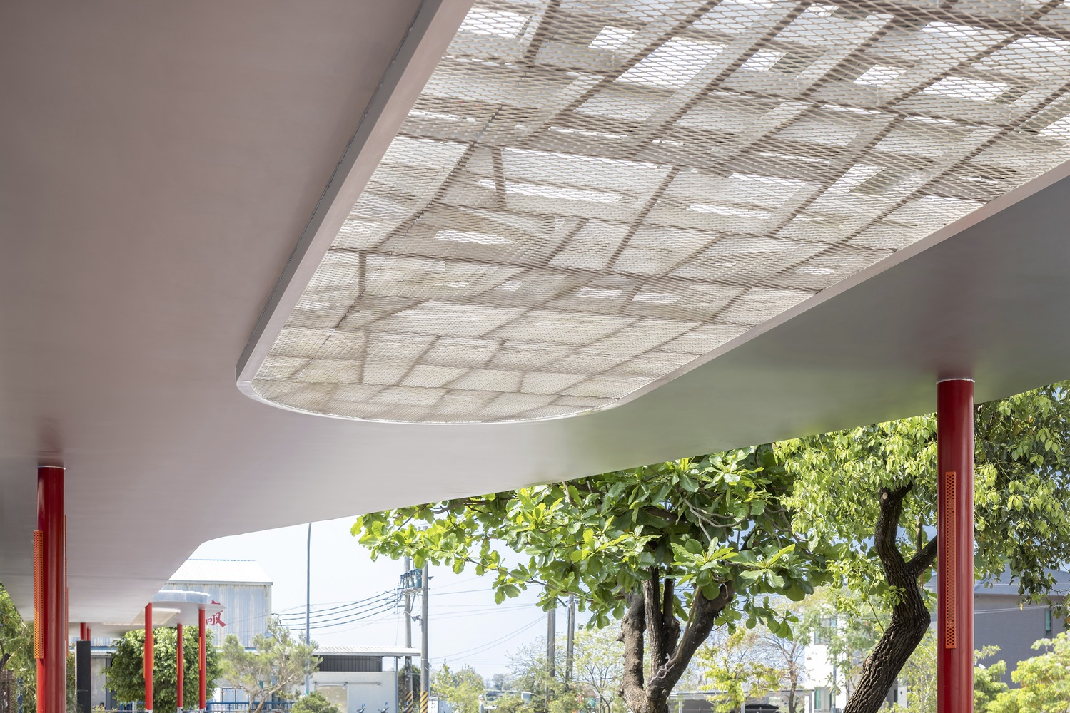 Ceiling detail: decorative metal screen panel with organic dragonfly-wing pattern, red column, tree canopy visible beyond