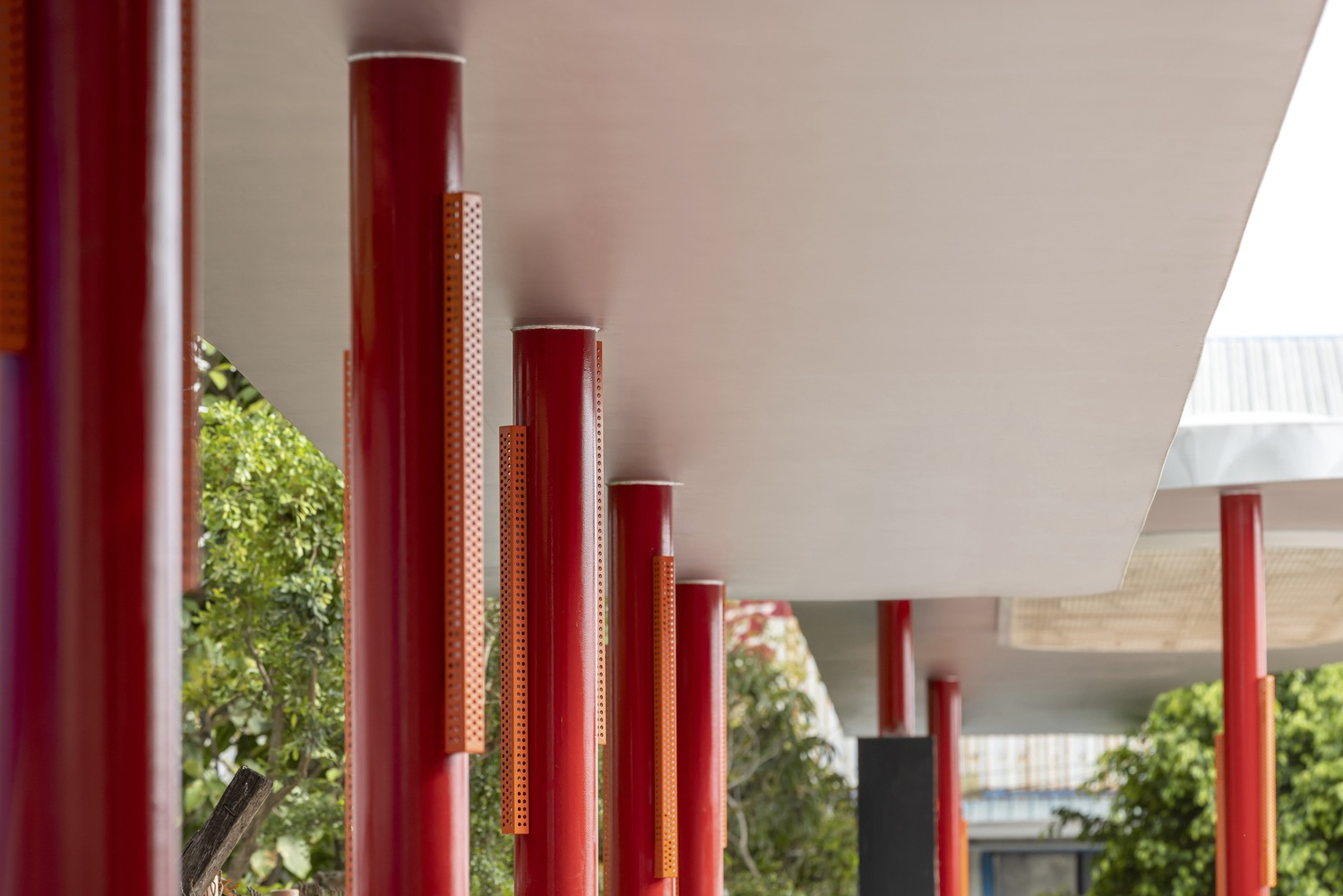 Red columns: close perspective along the colonnade, white canopy soffit above, greenery behind the railing