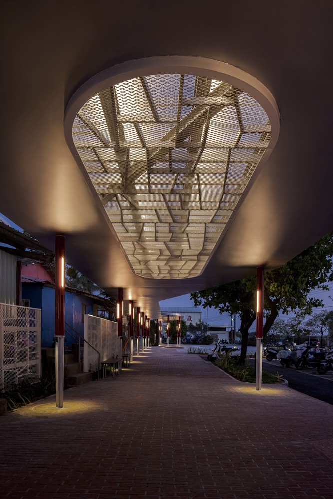 Night: walkway lit by bollard lights, oval skylight glowing warm from within, decorative screen pattern visible above