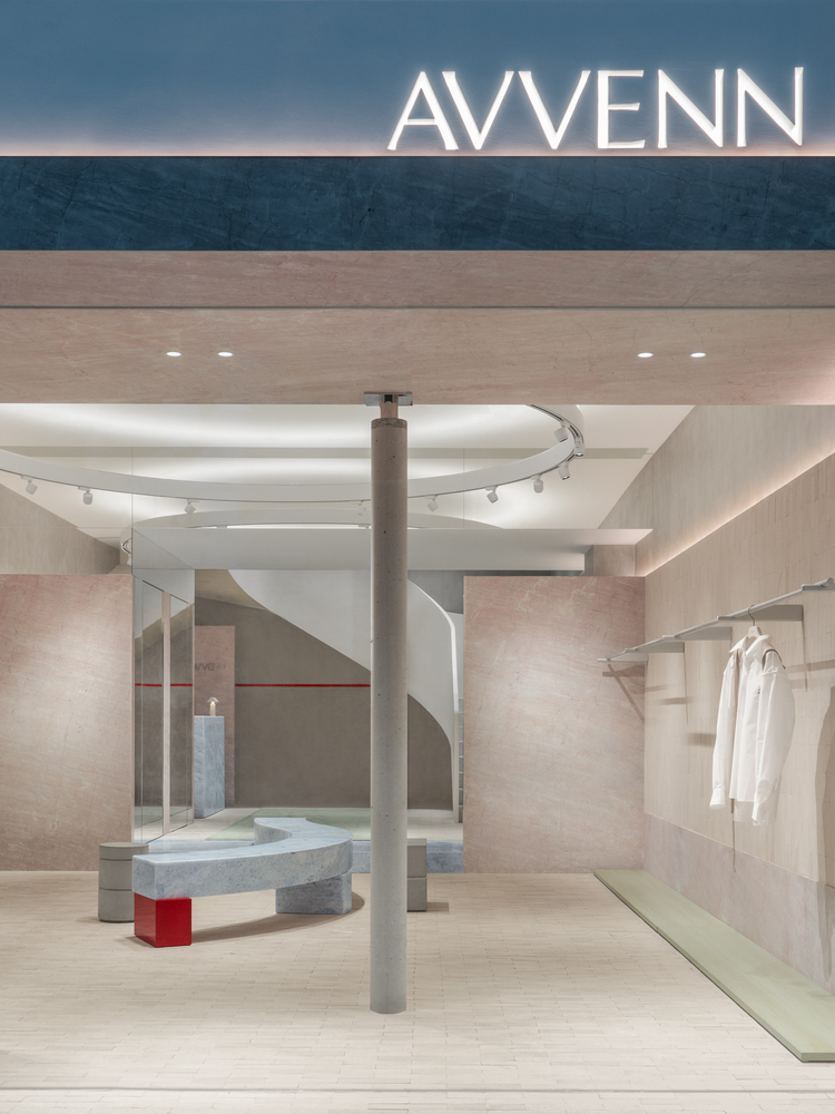 Retail interior with curved white staircase, pink stone walls, central column and curved stone seating element