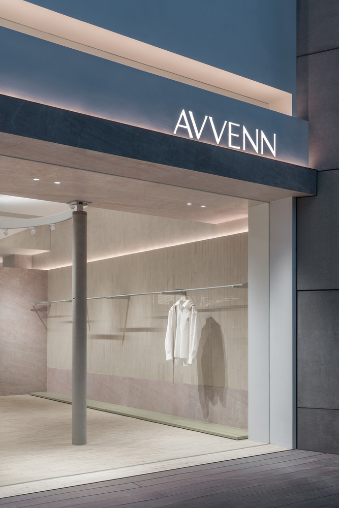 Storefront entrance at dusk with illuminated signage and view into interior with cylindrical column