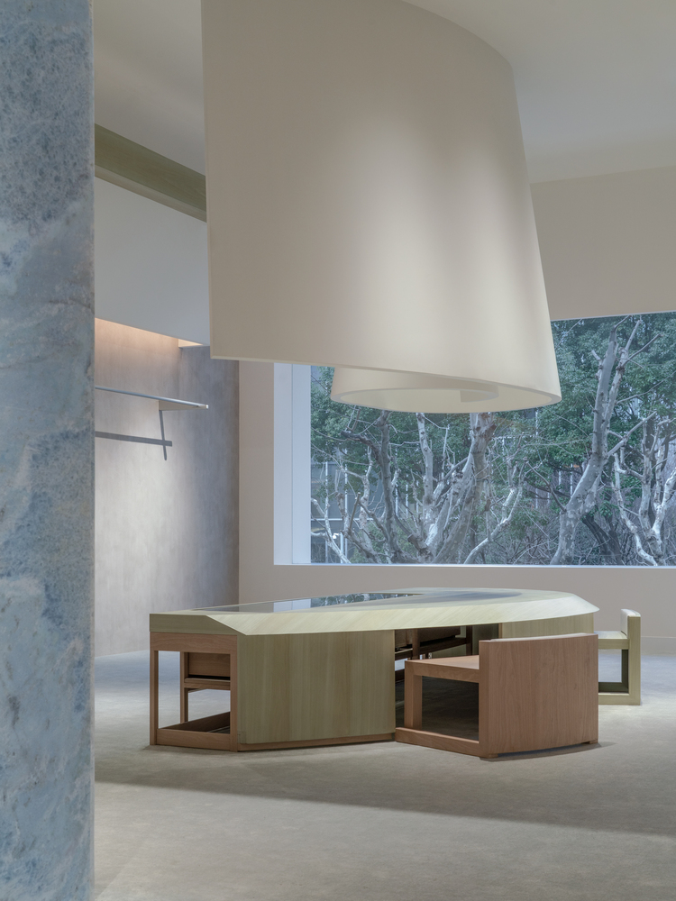 Timber table and seating platform beneath a tapered white ceiling element with trees visible through window