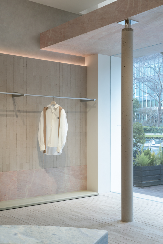 Interior retail space with glass display niche, exposed concrete column and floor-to-ceiling windows overlooking trees