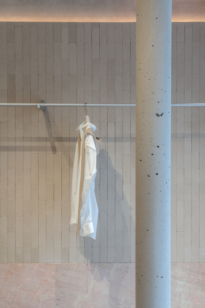 White garment hanging from a glass-enclosed display rail beside a cylindrical concrete column with tie marks