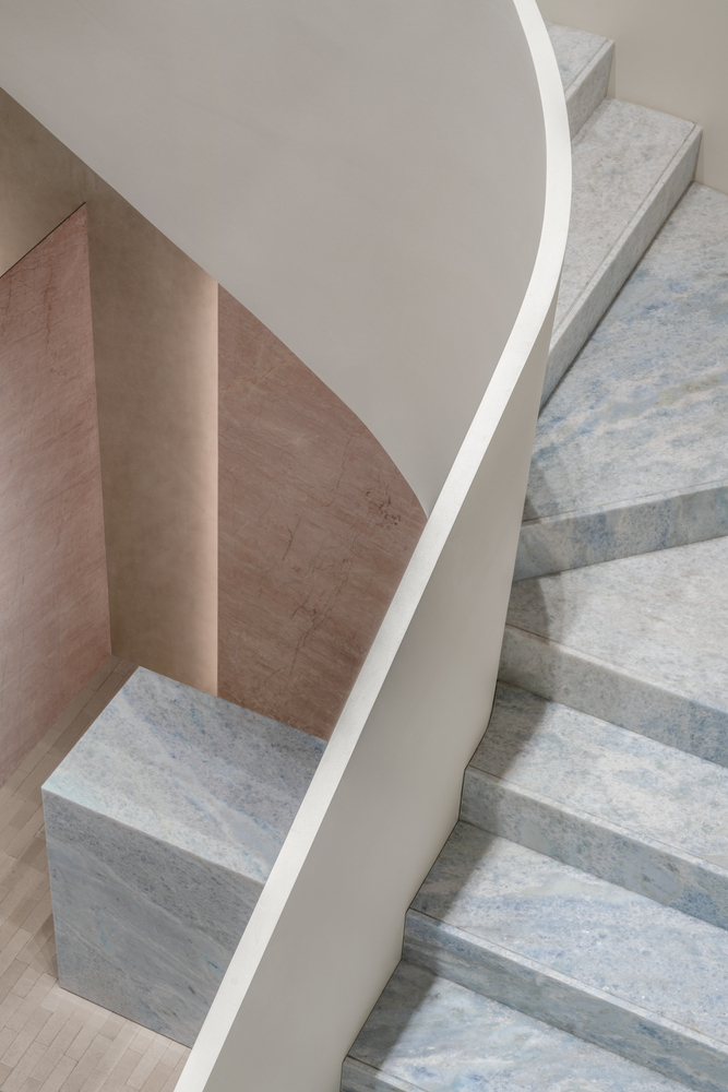 Detail of curved white balustrade meeting blue-veined marble stair treads and pink marble wall panels