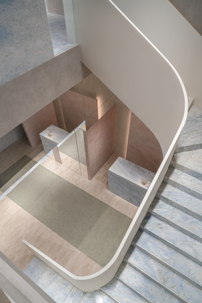 Overhead view of a spiraling staircase with blue marble treads and a curved white balustrade with integrated lighting