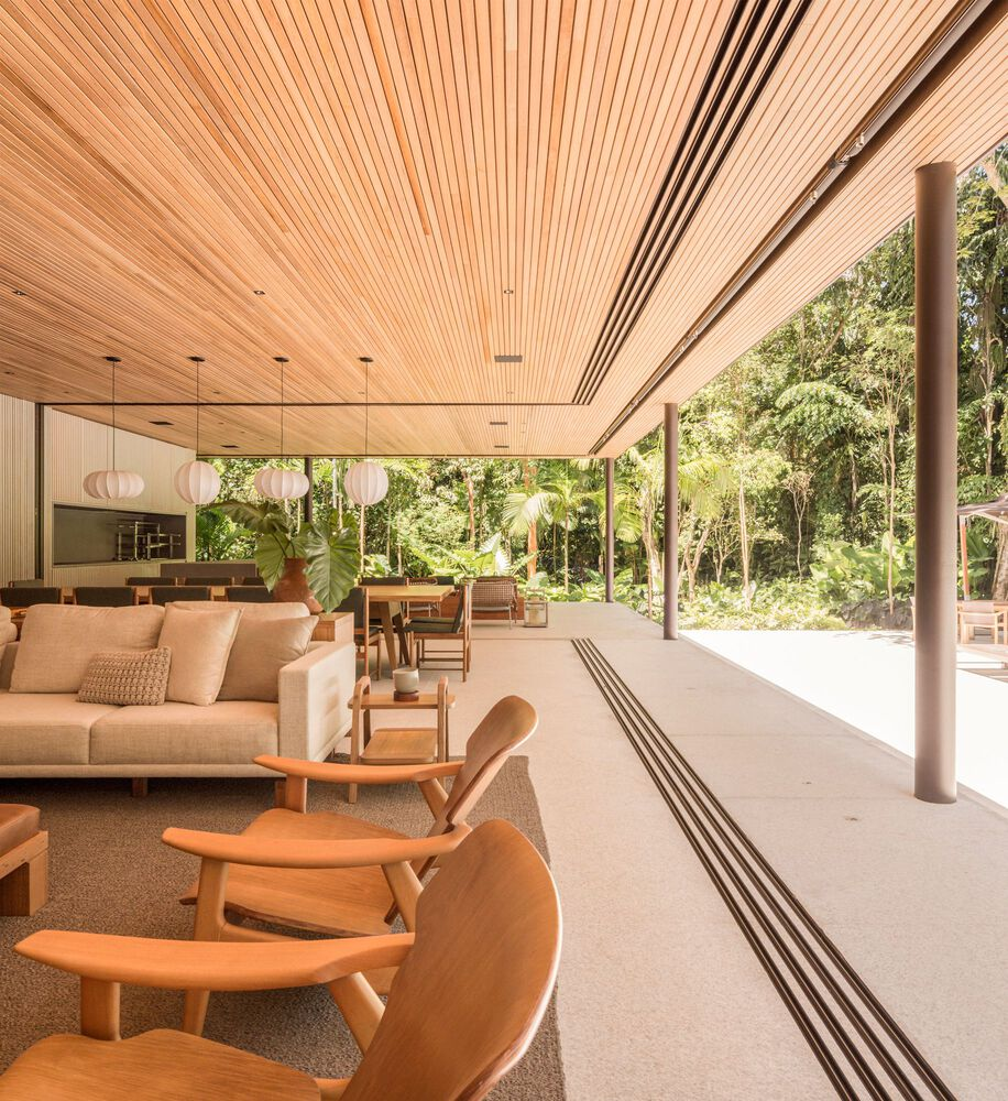 Open-plan living and dining: timber ceiling, cream sofa, leather lounge chairs, slatted timber screens, garden visible on all sides