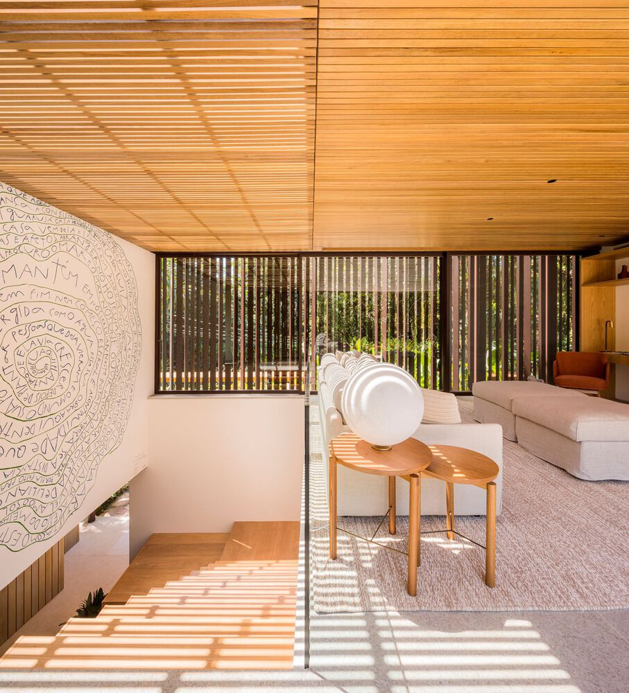 Sitting area: timber ceiling and vertical slatted screen, carved white relief wall panel, desk and chair, striped sunlight on floor