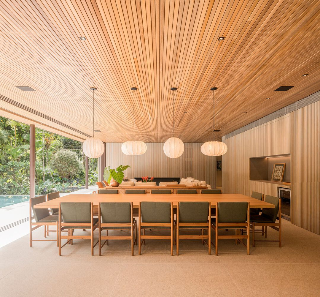 Dining room: long timber table, grey upholstered chairs, row of white paper globe pendant lamps, timber ceiling, glass walls