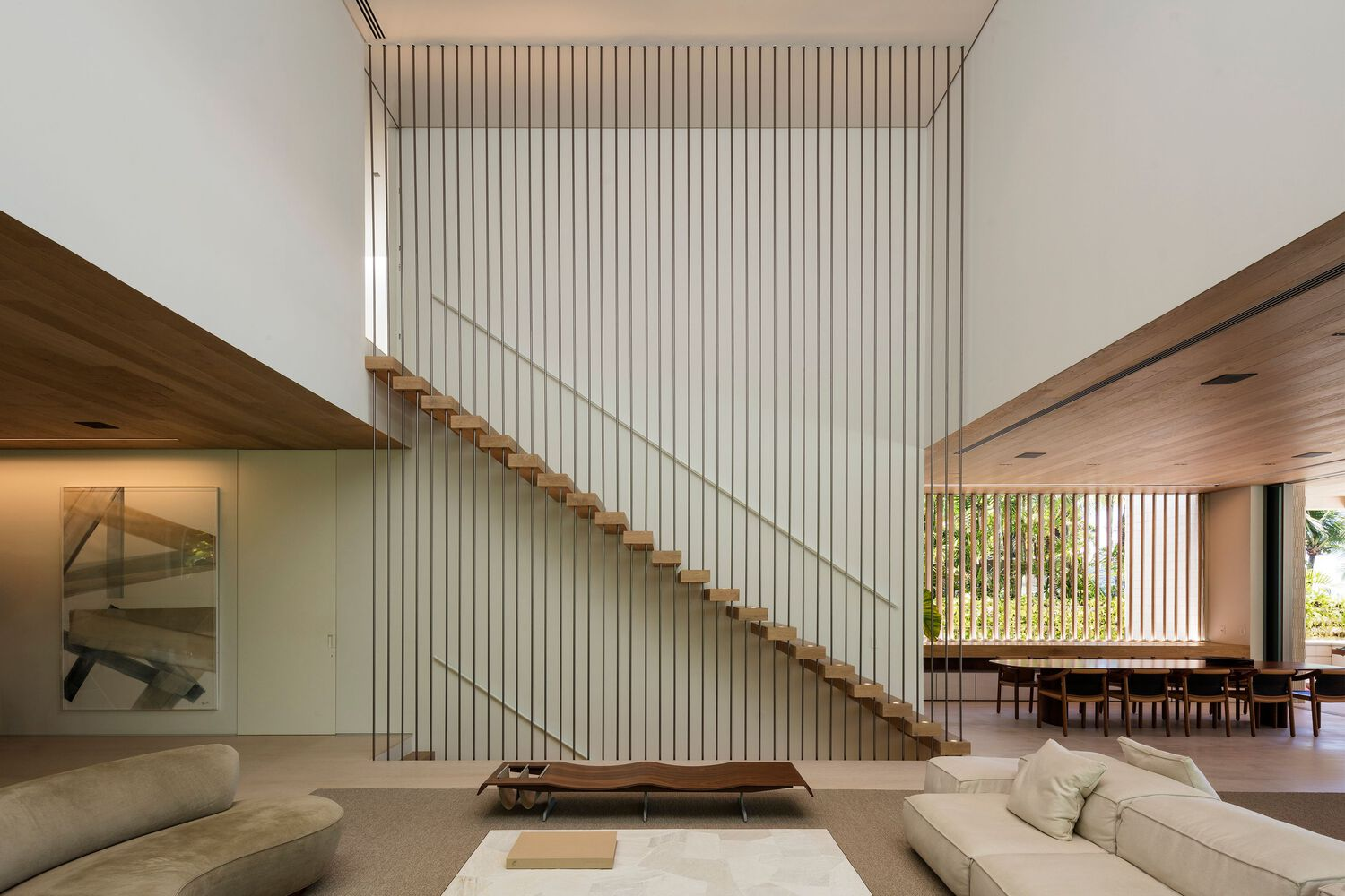 Floating timber staircase with wire balustrade ascending against a white vertical slat wall in daylight