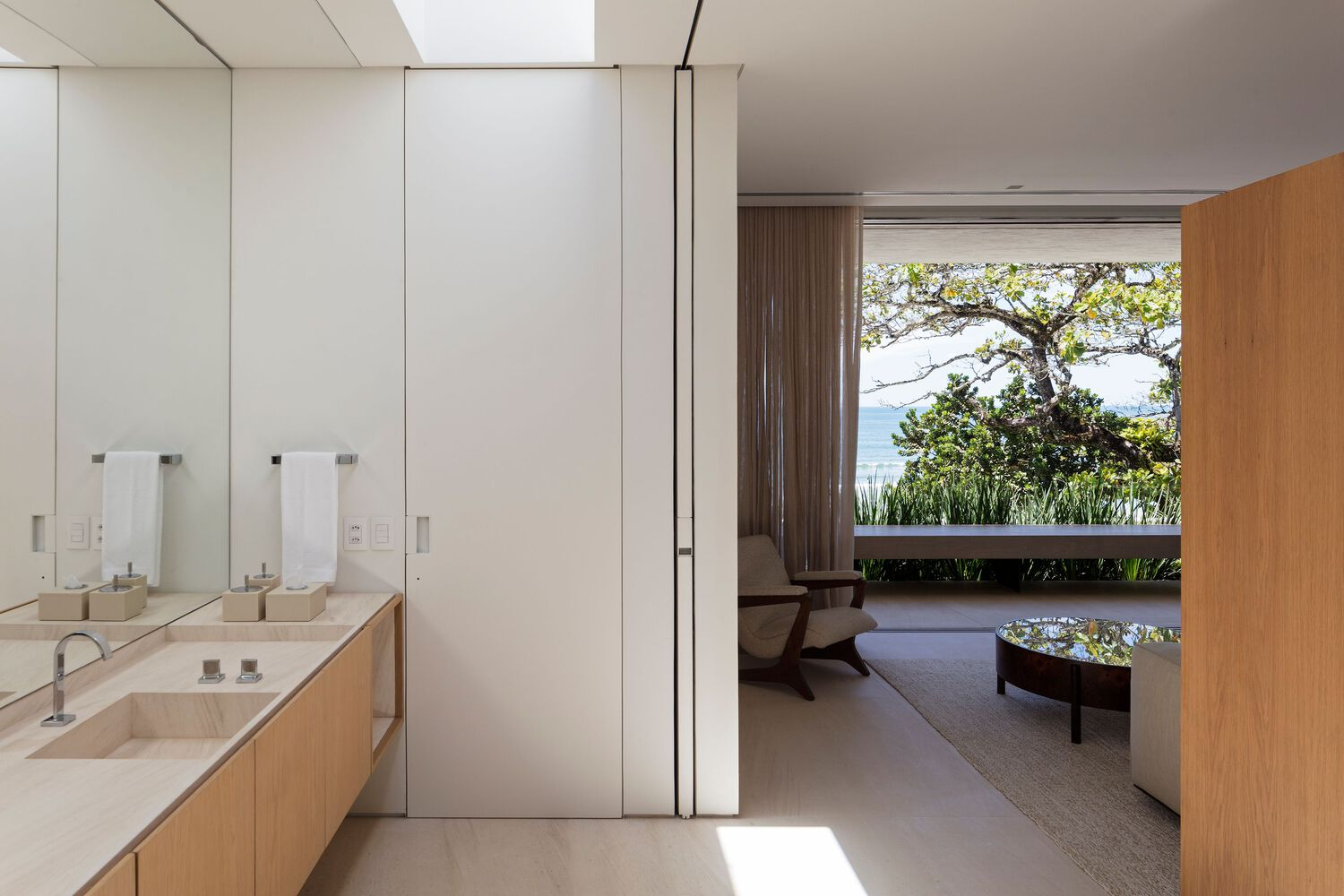 Bathroom vanity with white storage panels looking through to a terrace framed by trees and sky