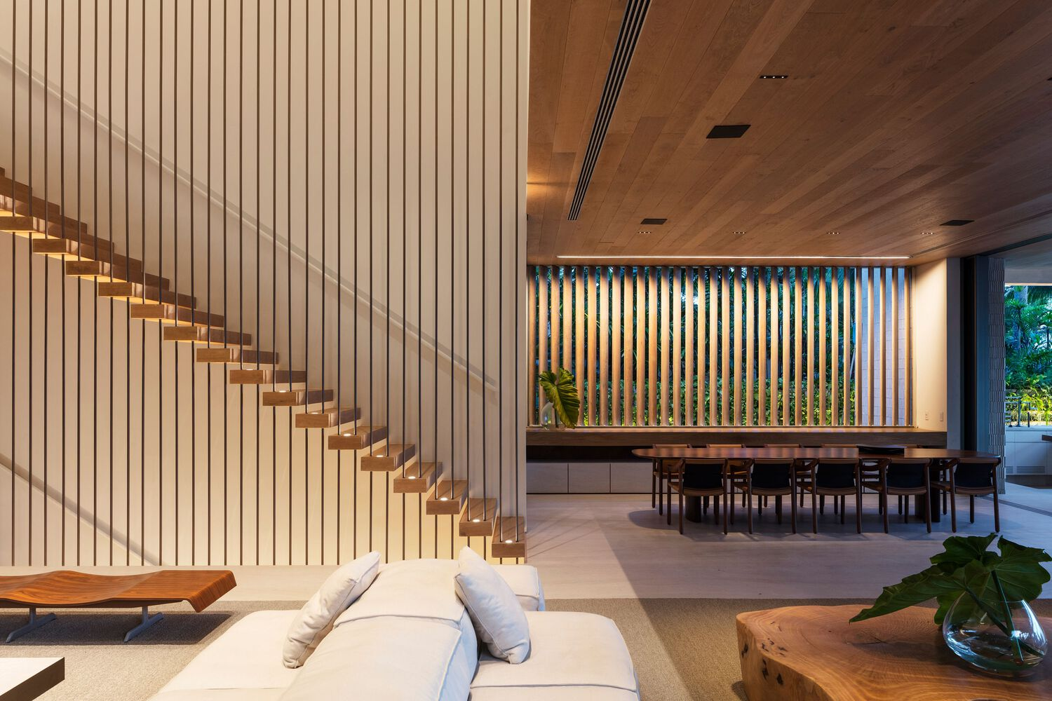 Open living space with floating timber staircase against vertical wood slat wall at dusk