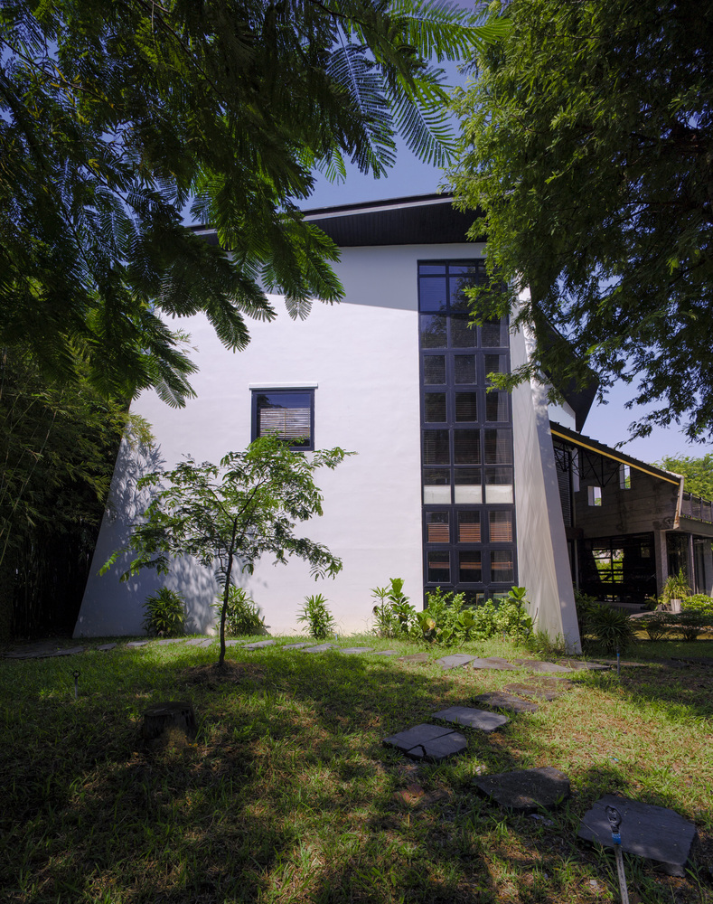White stucco facade with vertical ribbon window framed by overhanging trees and stepped stone path