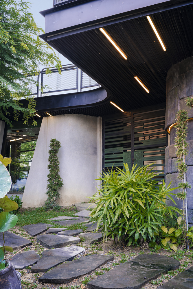 Covered entry with linear ceiling lights, concrete columns and irregular stepping stones through planted beds