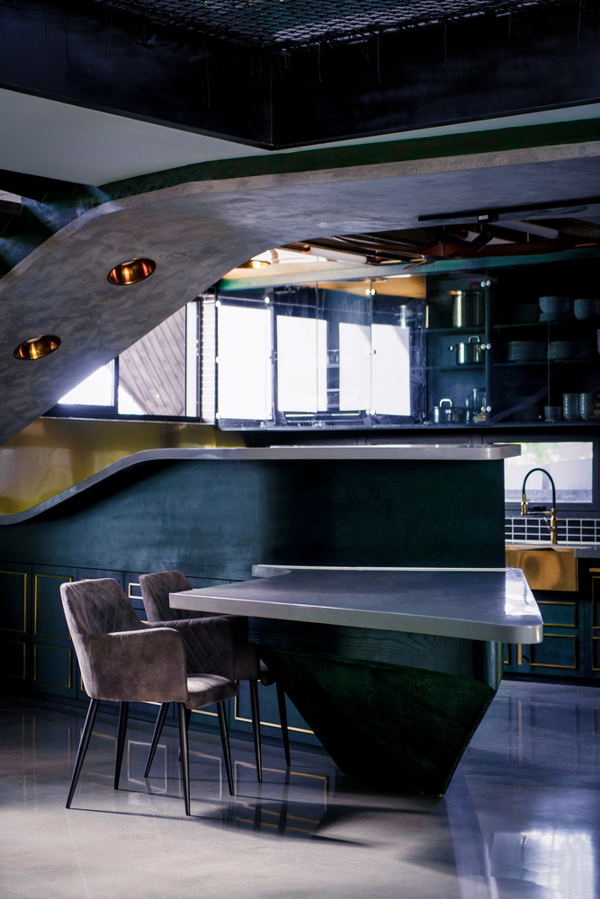 Kitchen island with dark green base and polished concrete top beneath a curved plaster ceiling with inset pendant lights