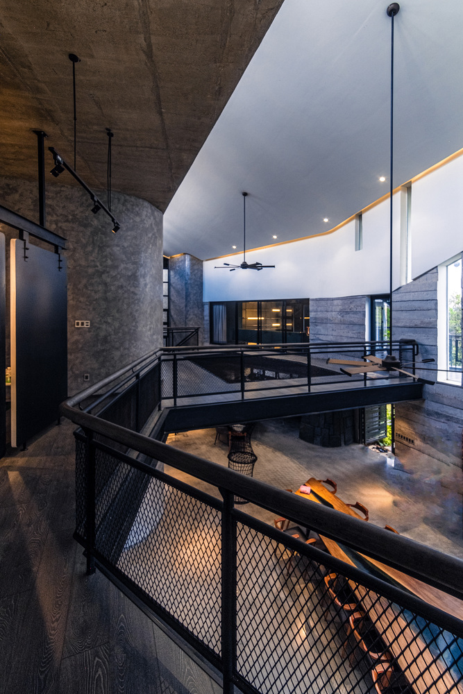 Mesh-floored mezzanine bridge crossing a central void with exposed concrete soffit and white plaster walls