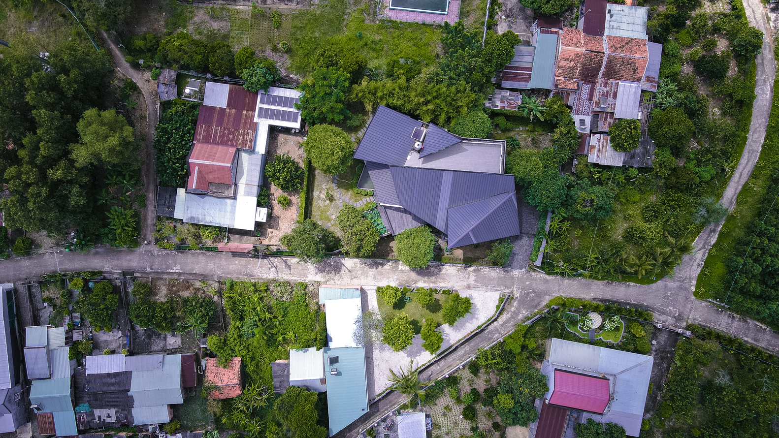 Aerial view of the angular metal roof among neighboring houses and dense tree canopy