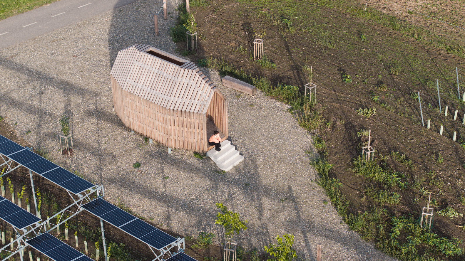 Aerial view of the barrel-vaulted timber structure with white entry steps beside solar panel array