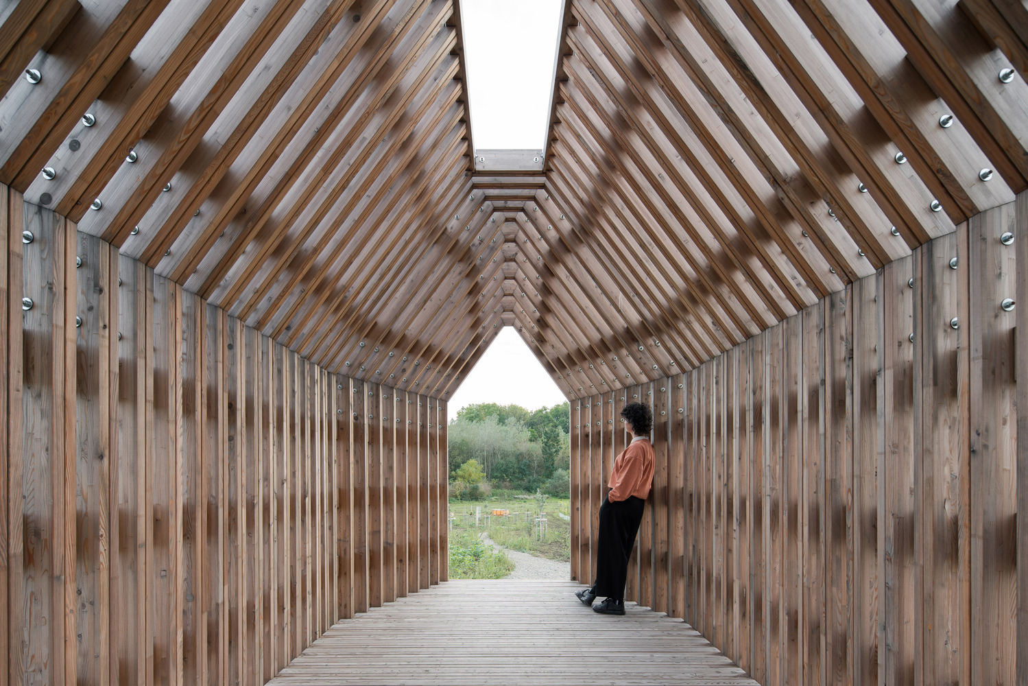 Interior view along timber slat corridor with vaulted ceiling skylight and person standing near opening