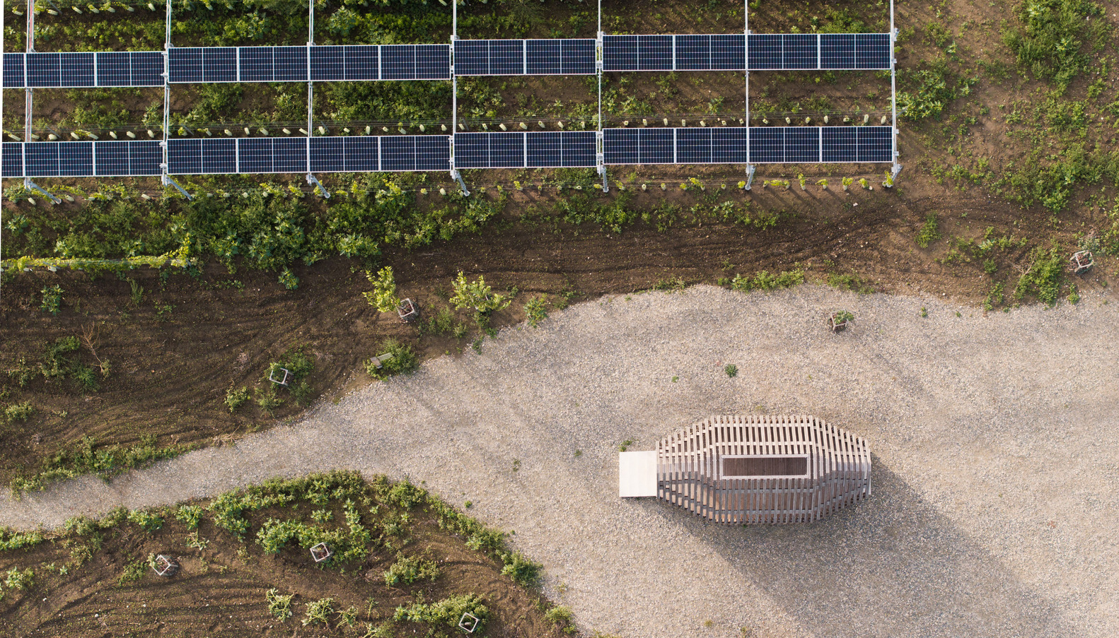Aerial view of a circular timber pavilion on gravel with solar panels and planted beds nearby