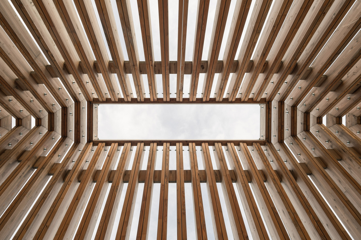 Looking up through the layered timber frame structure forming a rectangular skylight opening