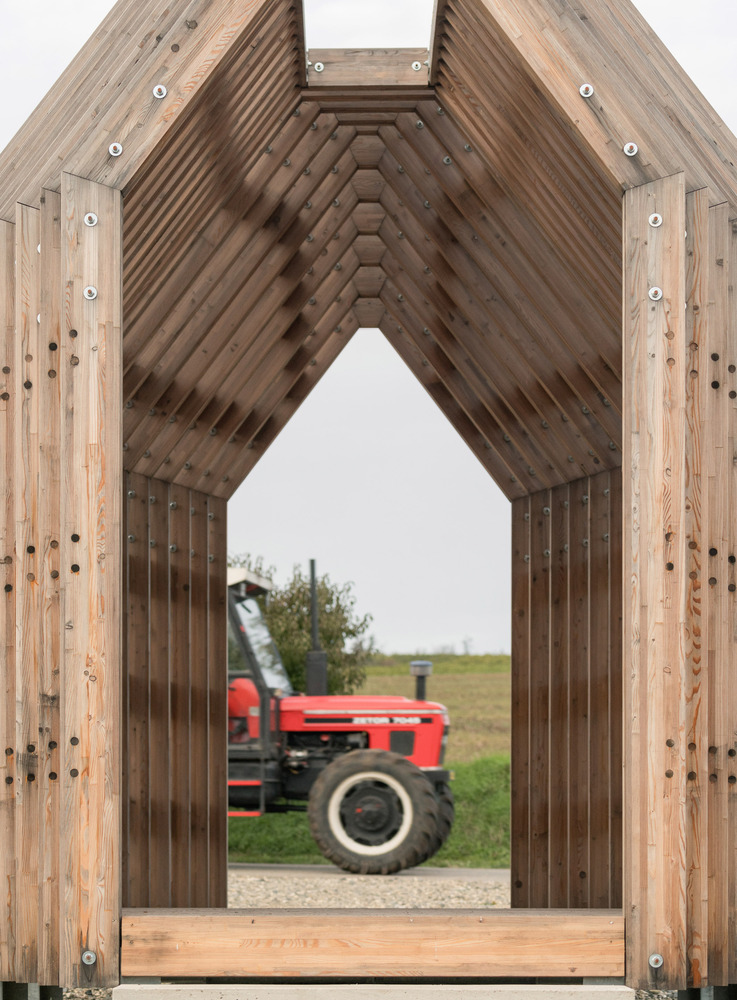 View through the pointed arch timber portal framing a red tractor in the field beyond
