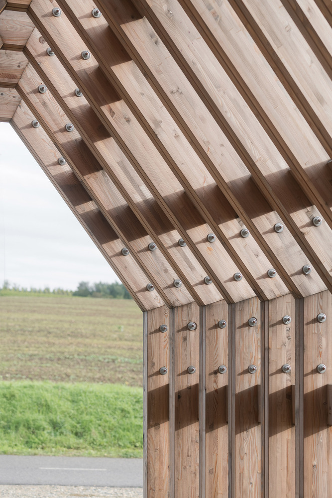 Detail of timber slat canopy with visible bolt fixings curving over agricultural fields