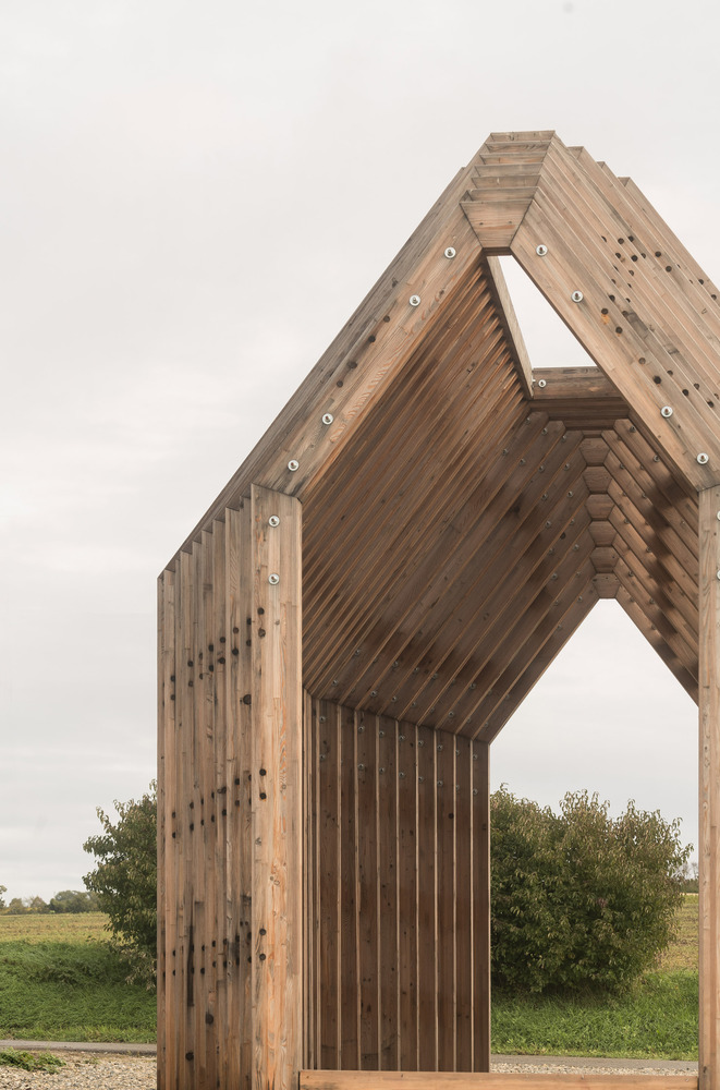 Upward view of the gabled timber pavilion with layered slat construction under overcast sky