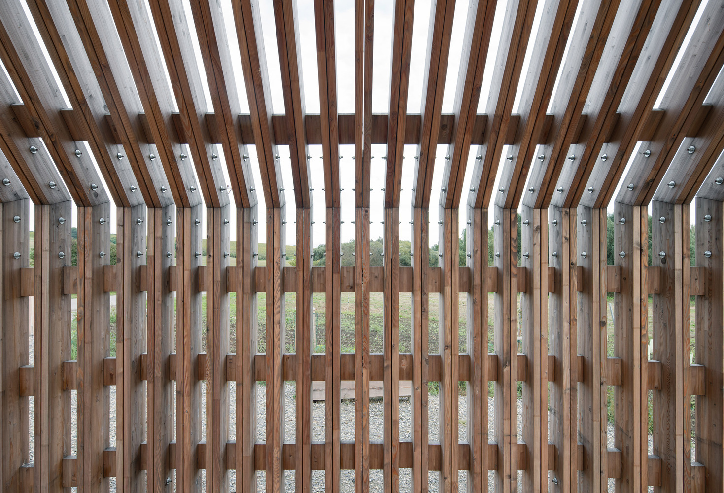 Interior view through timber slat walls with dappled light filtering onto gravel ground