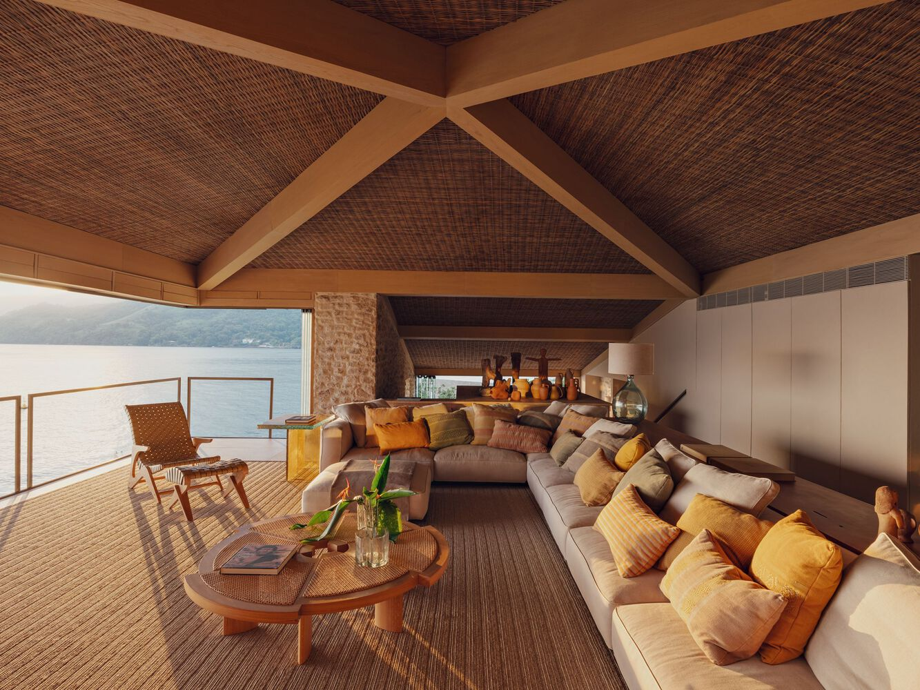Interior living space with woven ceiling and timber beams framing views of the lake beyond