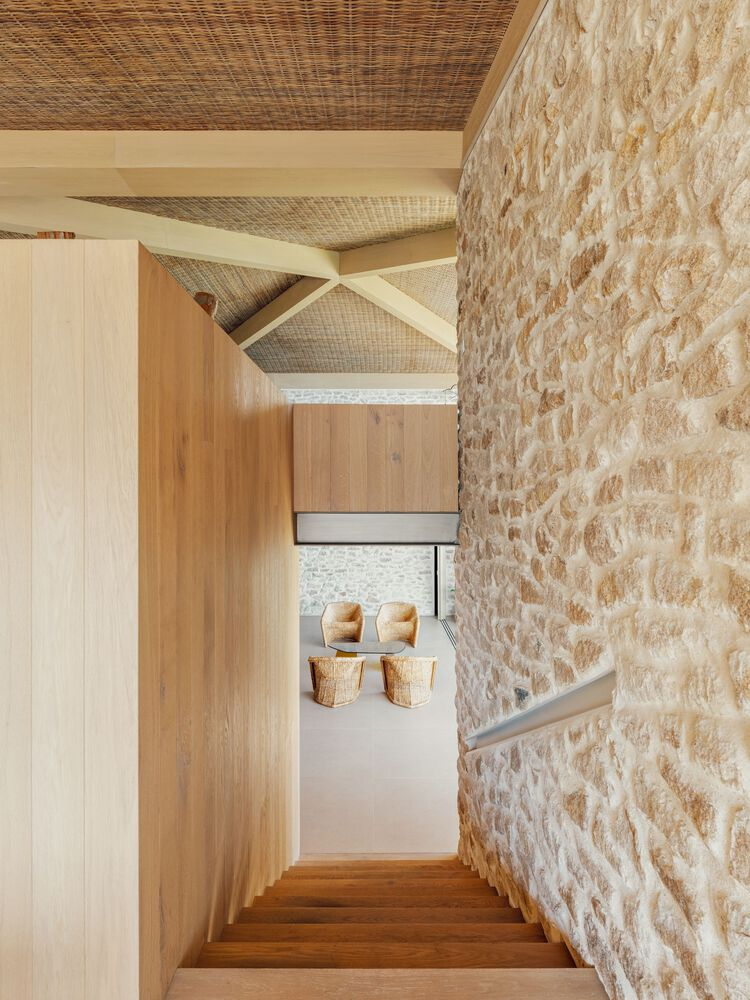 Timber stairwell descending past textured stone wall under exposed rafters and woven ceiling