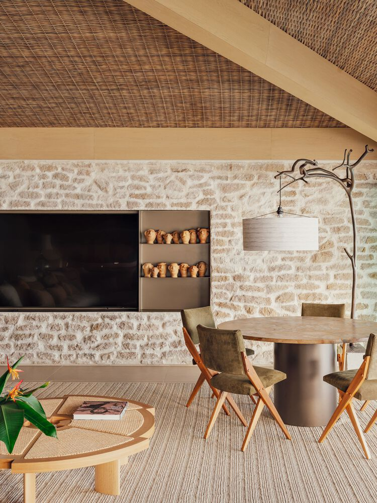 Living area with woven rattan ceiling, limestone wall, built-in shelves with ceramic pots, and timber beam