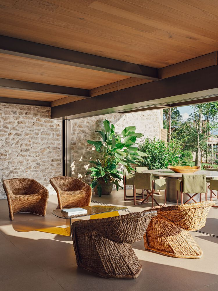 Open living space with woven seating, timber ceiling beams, stone wall, and sliding glass doors to garden