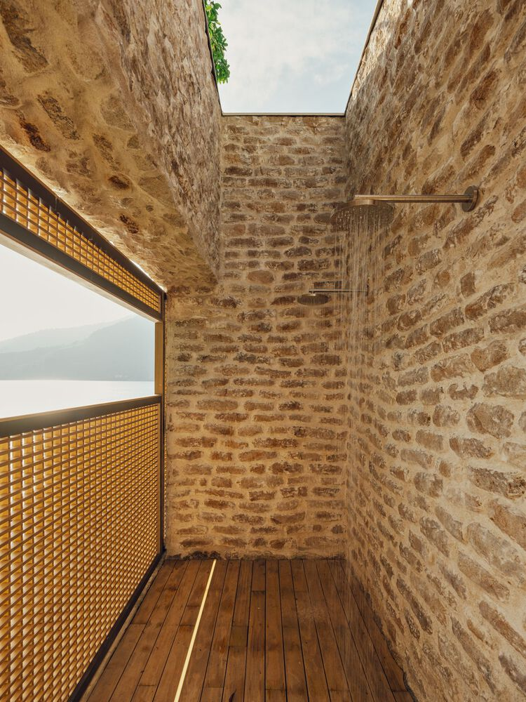 Outdoor shower enclosure with exposed stone walls, timber decking, and an open skylight above
