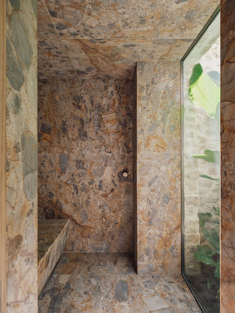 Stone shower enclosure with built-in bench and glazing overlooking banana leaves outside