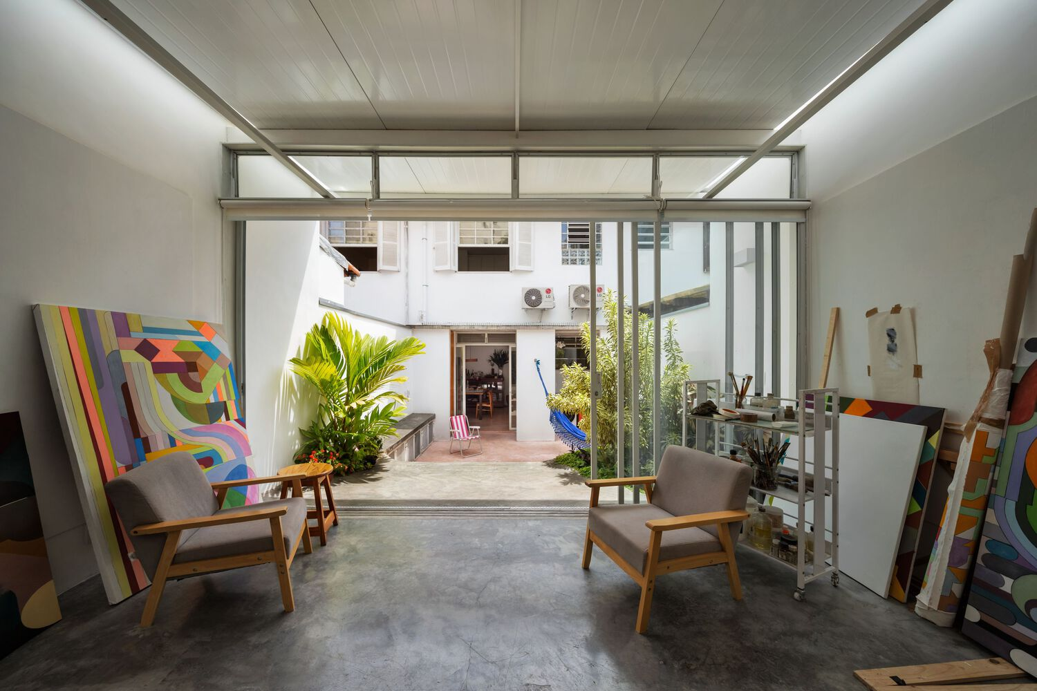 From the garden looking in: glass walls open, canvases visible inside, tree and planting in the foreground